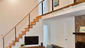 Un vaste salon doté d’un haut plafond, d’un escalier en bois, d’une cheminée et d’un téléviseur à écran plat fixé au mur.