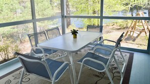 Une terrasse couverte avec une table et des chaises, une petite plante sur la table et une vue sur un lac et des arbres.