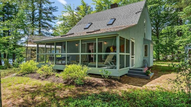 Une cabane aux parois vitrées, dotée d’un porche et entourée d’une végétation luxuriante et d’arbres.