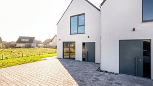 A modern two-story house with a large window and a garage door. - Cozy vacation home Elisa, house with fireplace, sauna, terrace, garden (Dranske-Lancken)