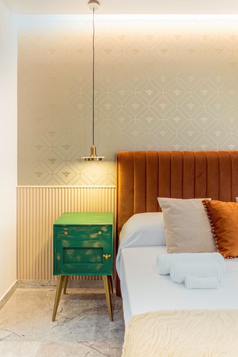 Ein Schlafzimmer mit einem Bett, einem grünen Nachttisch, einem Heizkörper und einer Wand mit Muster.
