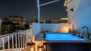 A rooftop terrace with a hot tub, candles, and a view of the cityscape at night.