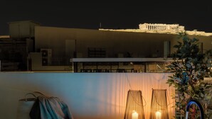 A rooftop terrace with a pool, seating area, and a view of ancient ruins in the background.