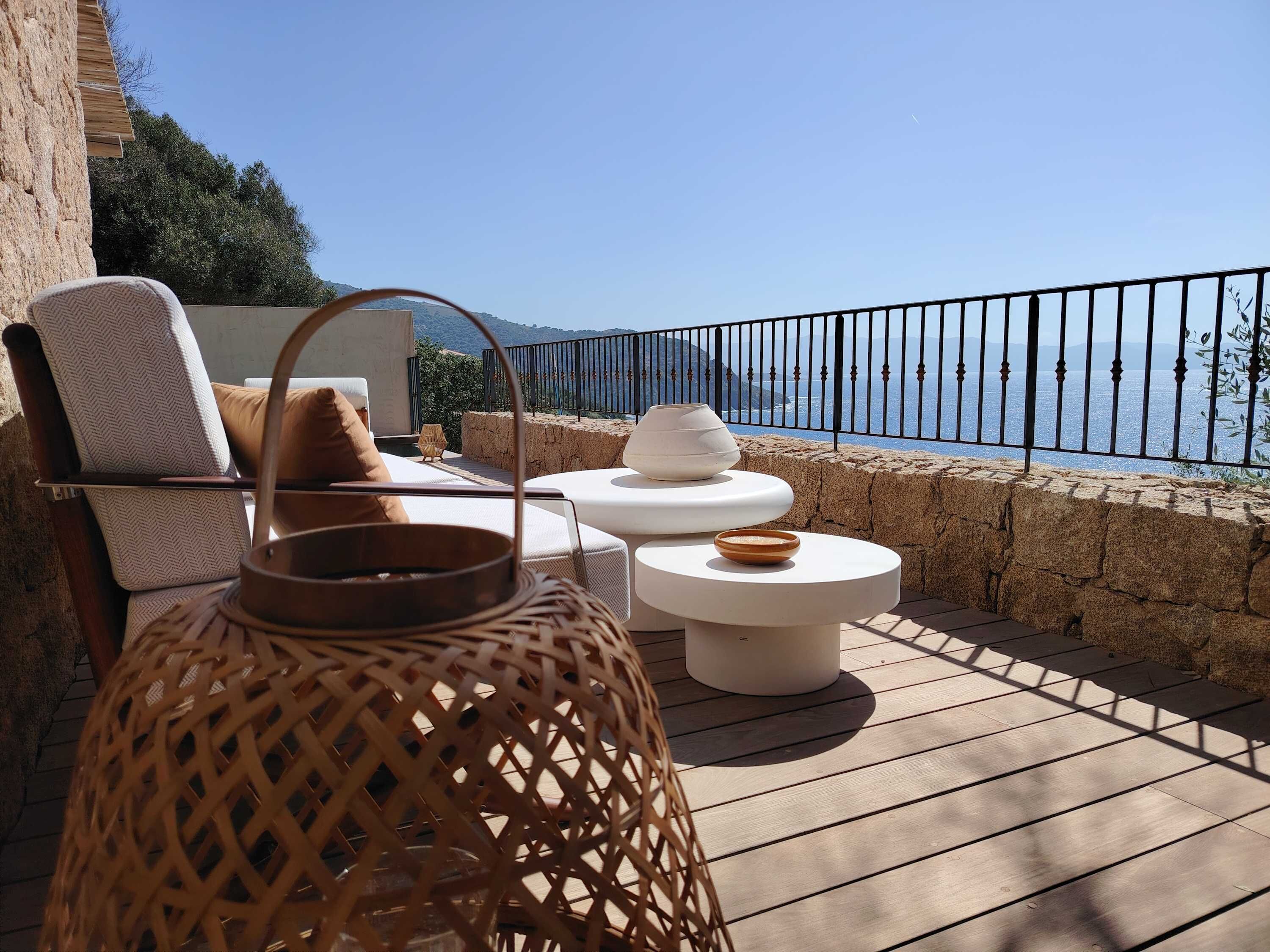 A terrace with a view of the sea, featuring a wicker chair, a white table, and a decorative bowl.