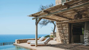 Zona junto a la piscina con sillones de descanso y una pérgola con vistas al mar.