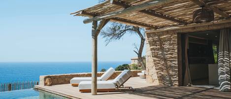A poolside area with lounge chairs and a pergola overlooking the sea.