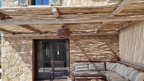 Una casa de piedra con porche cubierto, puerta de cristal y una zona de estar con cojines.