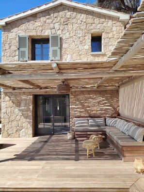A stone house with a covered patio, a glass door entrance, and a seating area with cushions.