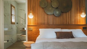 Un dormitorio con cabecera de madera, una cama grande con ropa blanca, dos luces empotradas en la pared y un panel de madera con adornos circulares.
