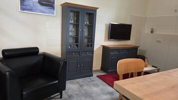 Ein Wohnzimmer mit einer schwarzen Ledersofa, einem Holzes Esstisch, einem roten Teppich, einer dunkelblauen Schrank mit Glastüren und einem an der Wand befestigten Flachbildfernseher.