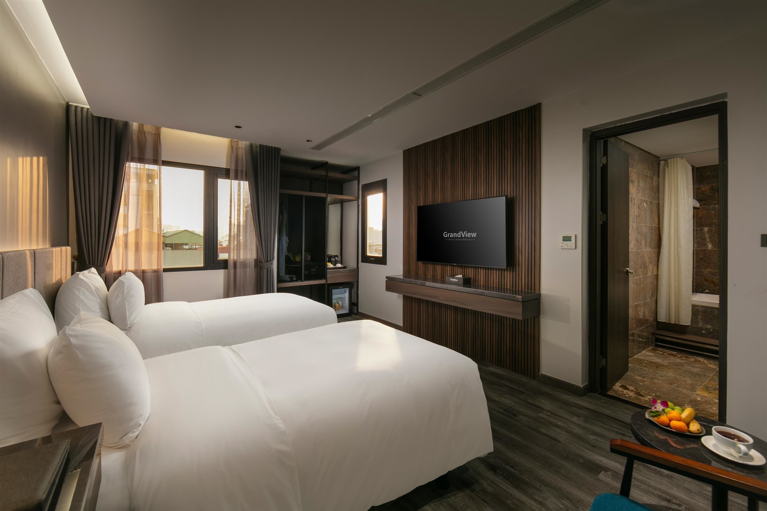 A hotel room with two beds, a TV, a small desk with a coffee cup, and a fruit plate.