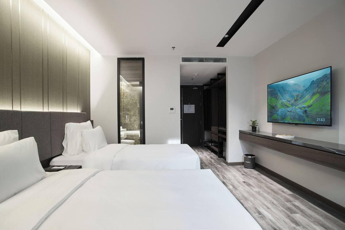 A modern hotel room with two beds, a flat-screen TV, and a view of a mountainous landscape.