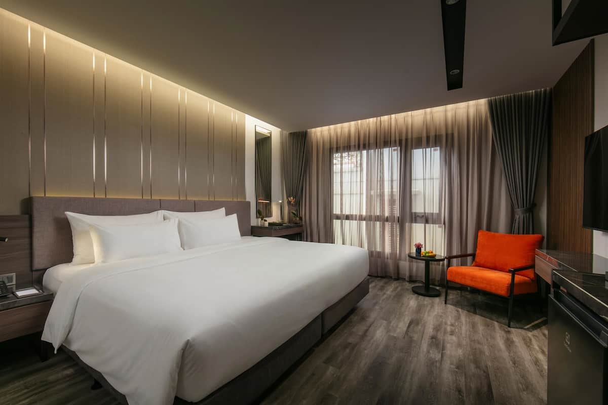 A modern hotel room with a large bed, a nightstand, a desk with a chair, a TV, and a window with curtains.