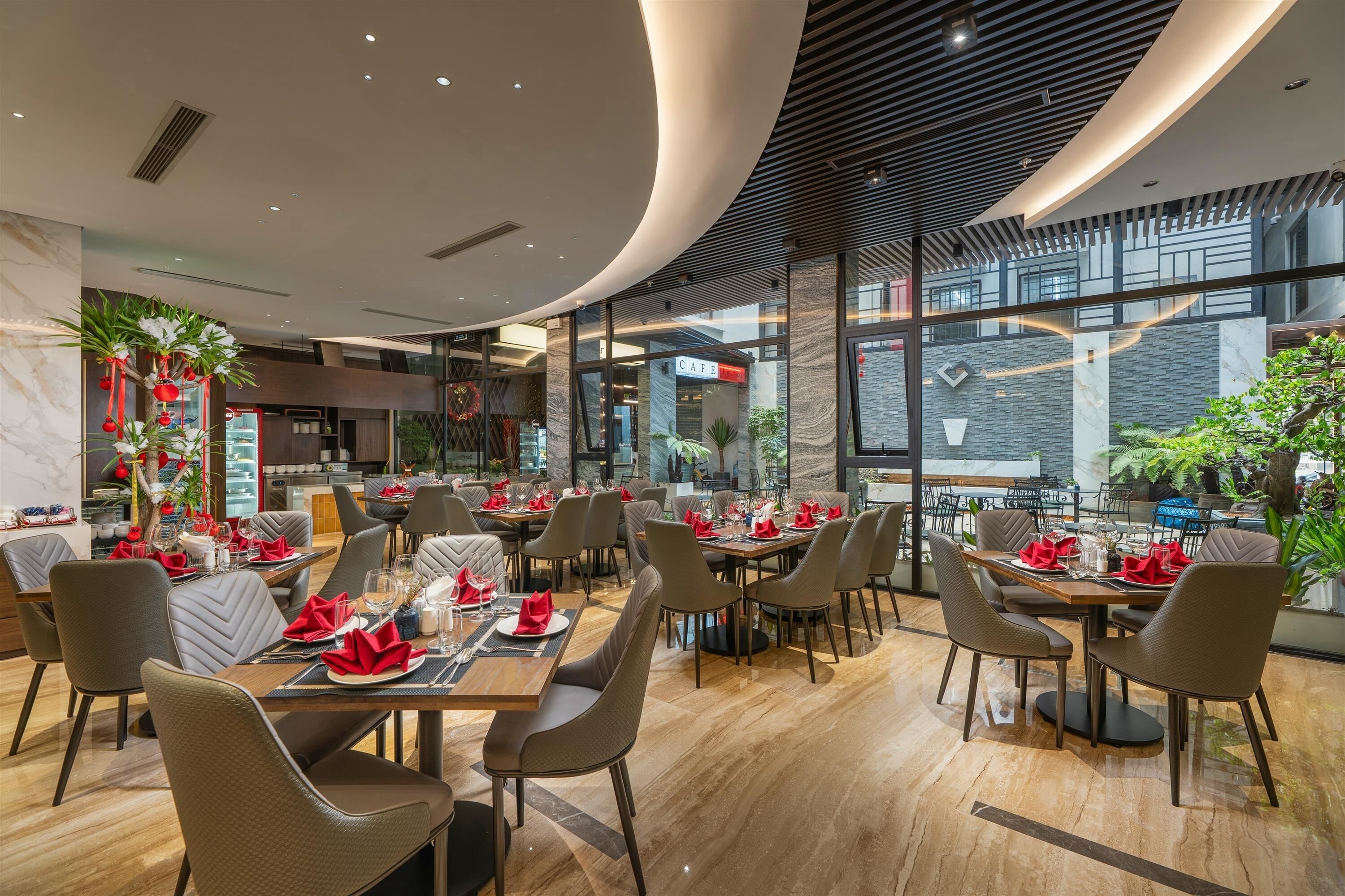Un restaurante moderno con varias mesas, cada una con servilletas y cubiertos rojos, y un amplio ventanal que ofrece vistas al exterior.