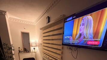 Une chambre d’hôtel avec un téléviseur fixé au mur, une table à manger avec une télécommande, un miroir et un radiateur.