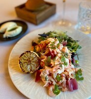 Un plato de comida con camarones, vegetales verdes y una rodaja de limón.