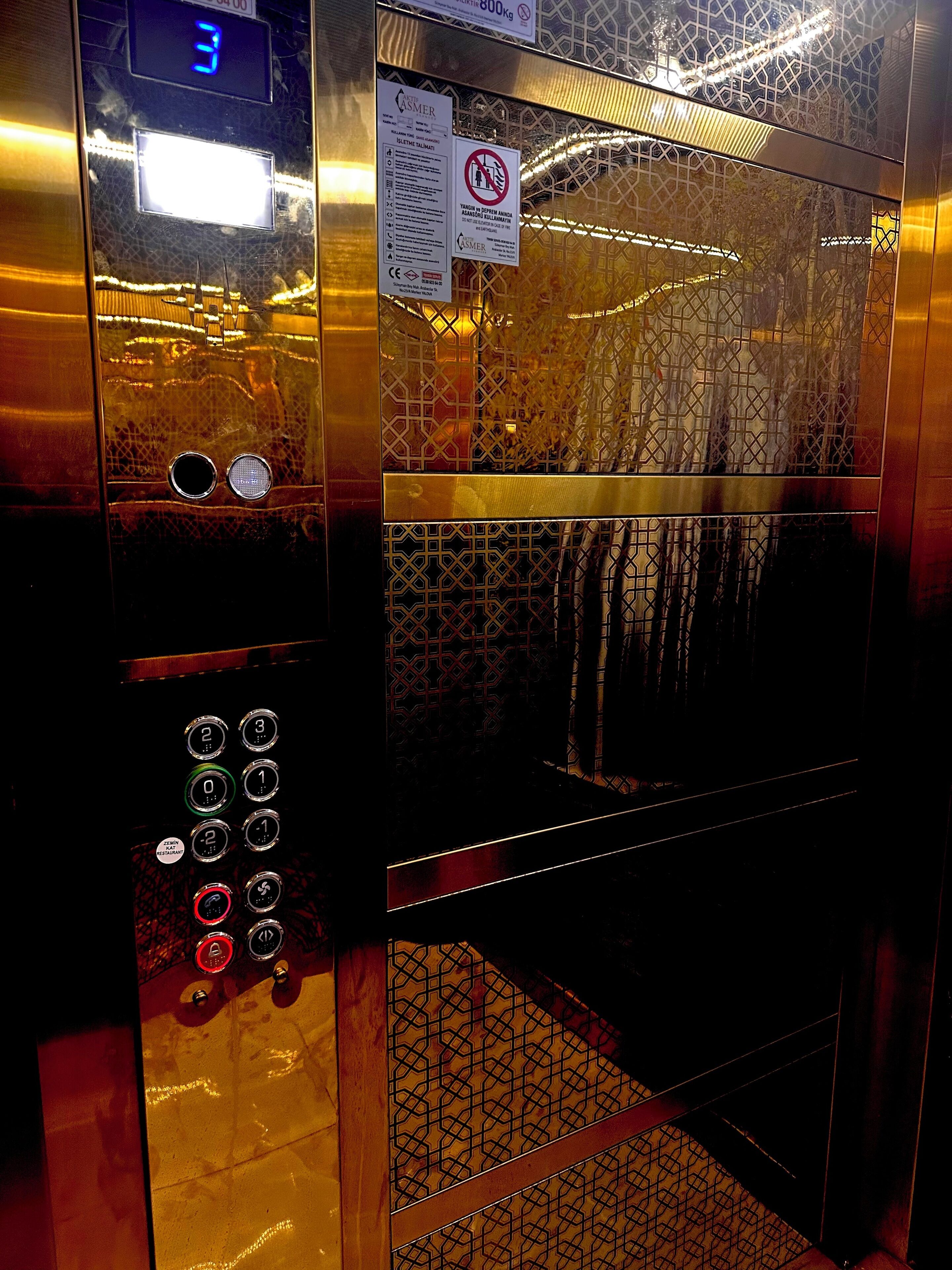 An elevator interior with a digital display, control buttons, and a safety sign.