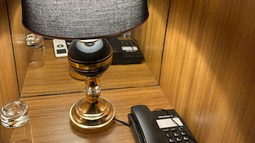 Una mesita de noche de madera con una lámpara, un teléfono y un control remoto.