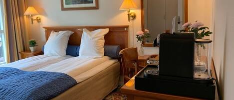 Ein Hotelzimmer mit einem Bett, Nachttischlampen, einer Kaffeemaschine, einem Spiegel und einem kleinen Tisch mit einem Blumenvasen.