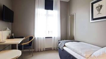 Una habitación de hotel con cama, escritorio, silla, televisor y ventana con cortinas.