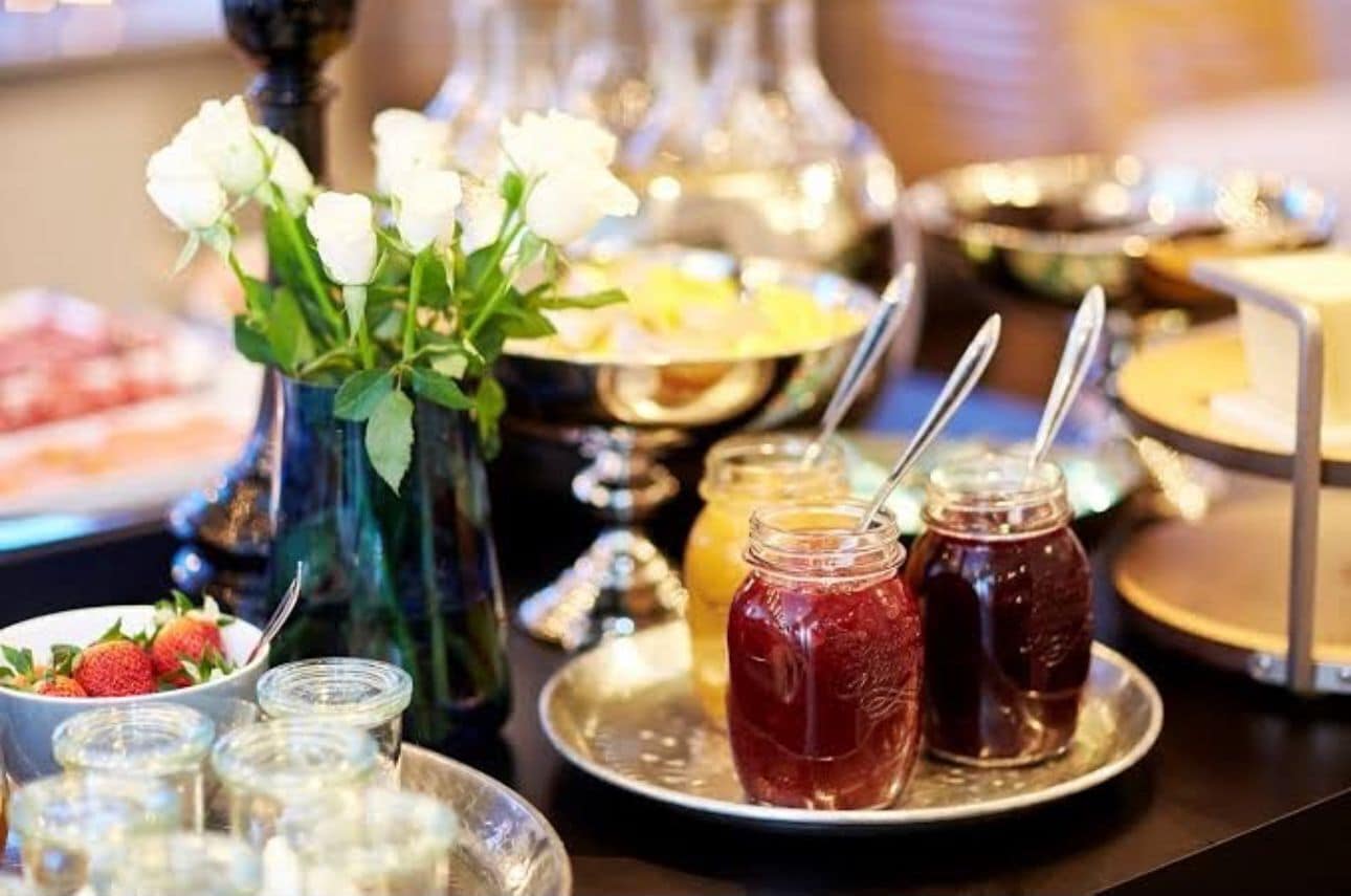 A buffet with various food items, including strawberries, and two jars of red jam.