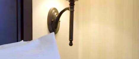 A neatly made bed with white linens, a wall-mounted lamp, and a vase with flowers on a bedside table.