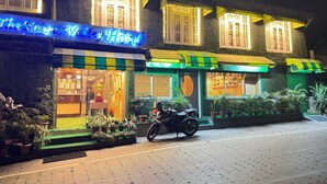 A hotel with a neon sign, a motorcycle parked in front, and potted plants around the entrance. - The Kaizer Valley Hotel (Kurseong)