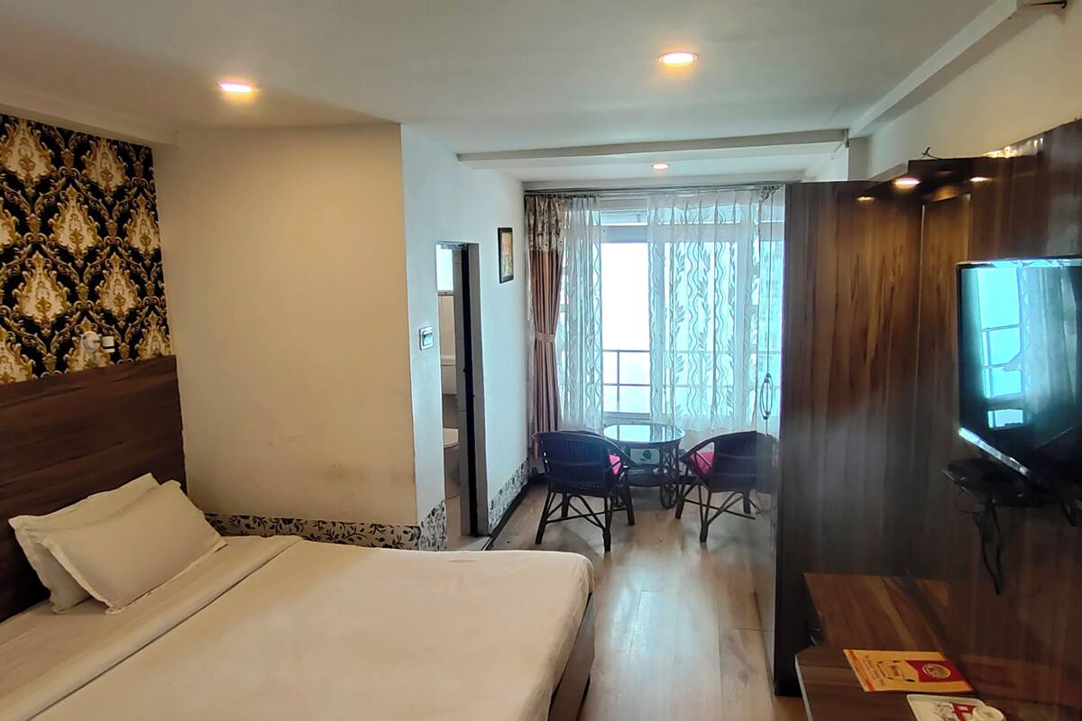 A hotel room with a bed, a television, a small table, and a window with curtains.