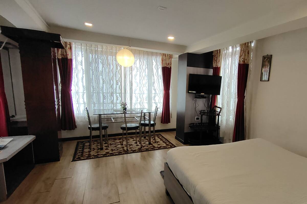 A hotel room with a bed, a desk with a chair, a TV, and a window with curtains.