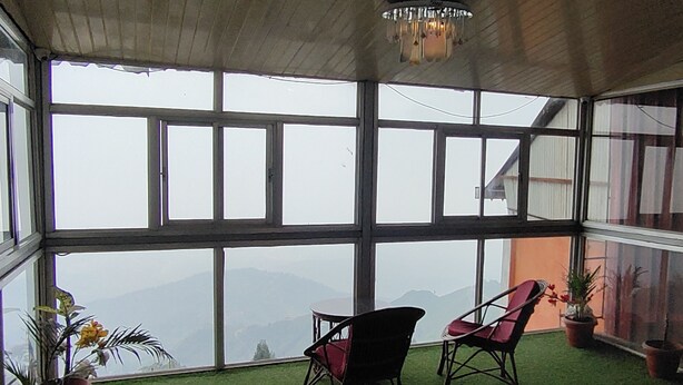 A room with large windows, a chandelier, two chairs, and potted plants. - The Kaizer Valley Hotel (Kurseong)