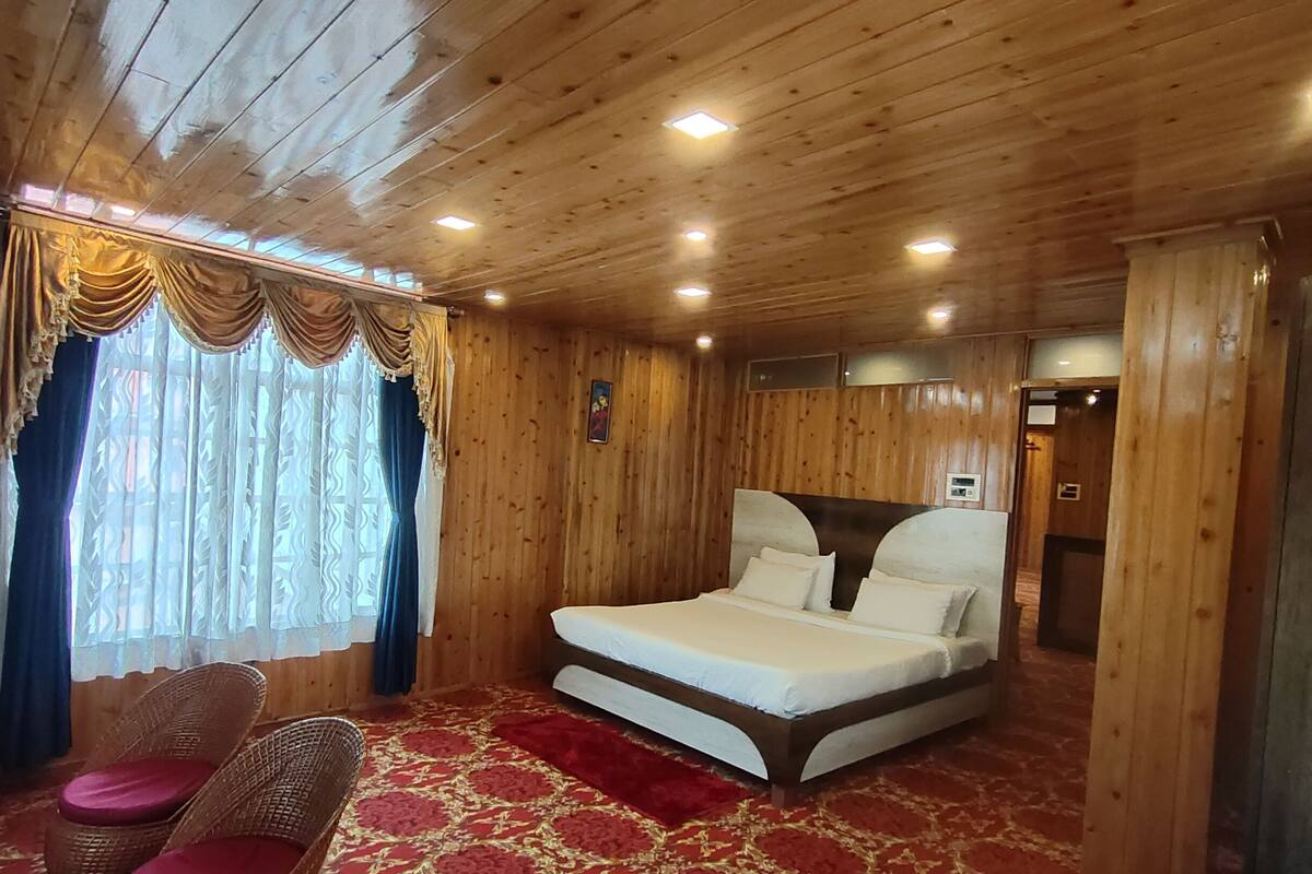 A wooden cabin room with a bed, a chair, and a window with curtains.
