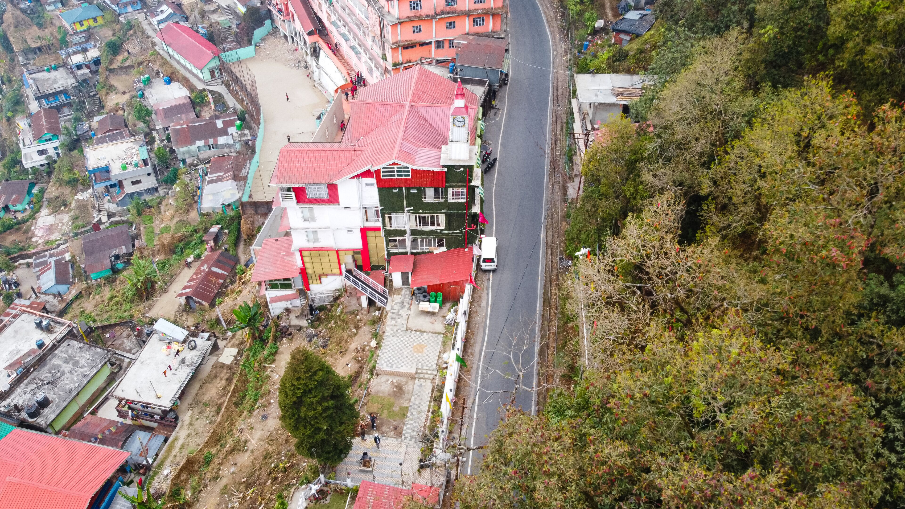 An aerial view of a residential area with houses, a road, and a hill with dense vegetation.
