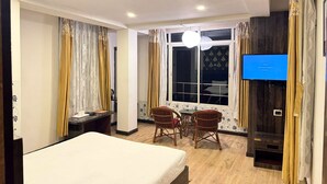 A hotel room with a bed, a desk, a chair, a table, and a TV. - The Kaizer Valley Hotel (Kurseong)