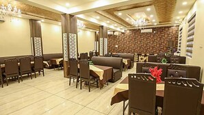 A spacious dining area with multiple tables and booths, featuring a patterned wall and a chandelier. - Sandalwood (Meerut)