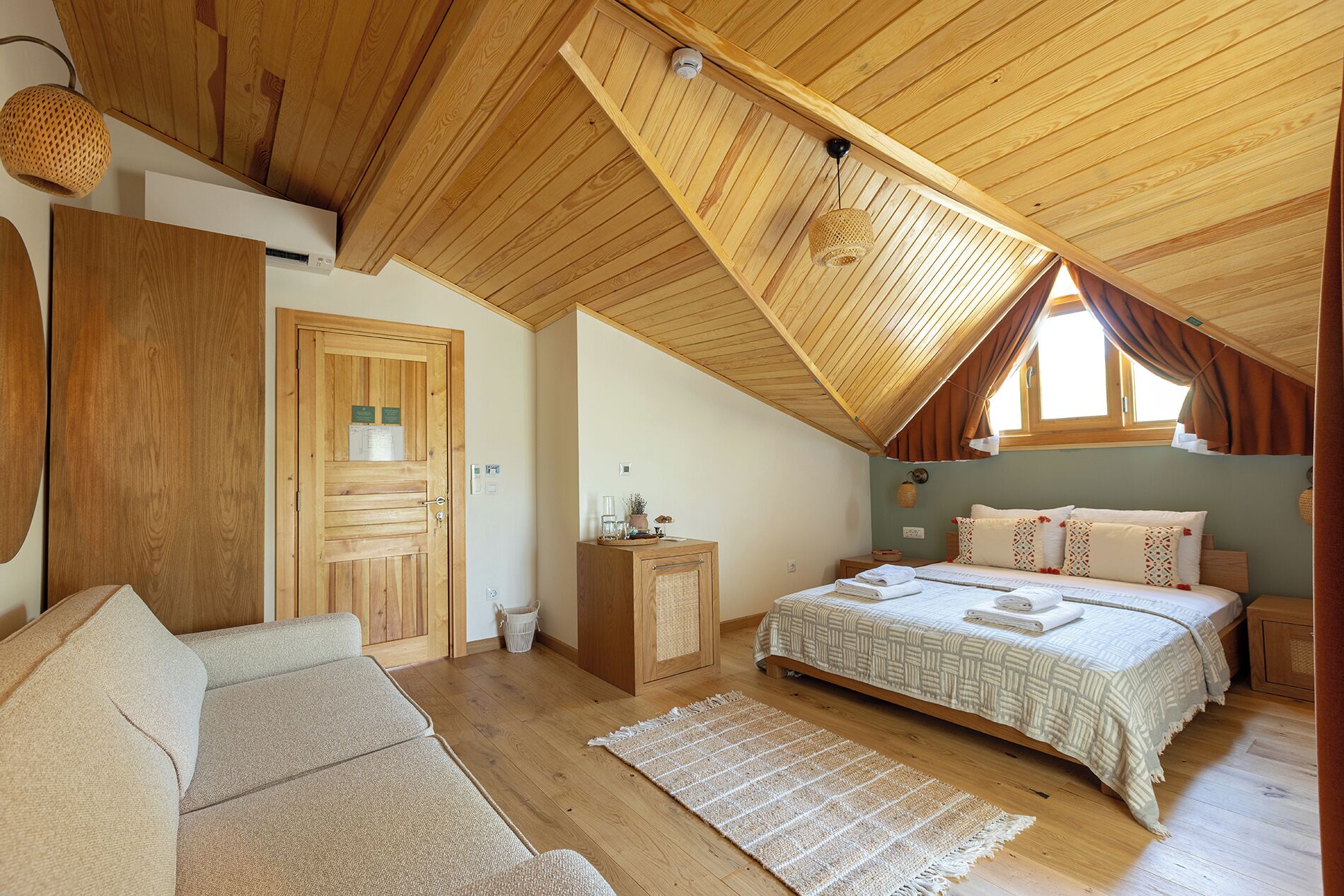 Un dormitorio acogedor con techo de madera, una cama con colcha estampada, un pequeño armario de madera y una lámpara de mimbre.
