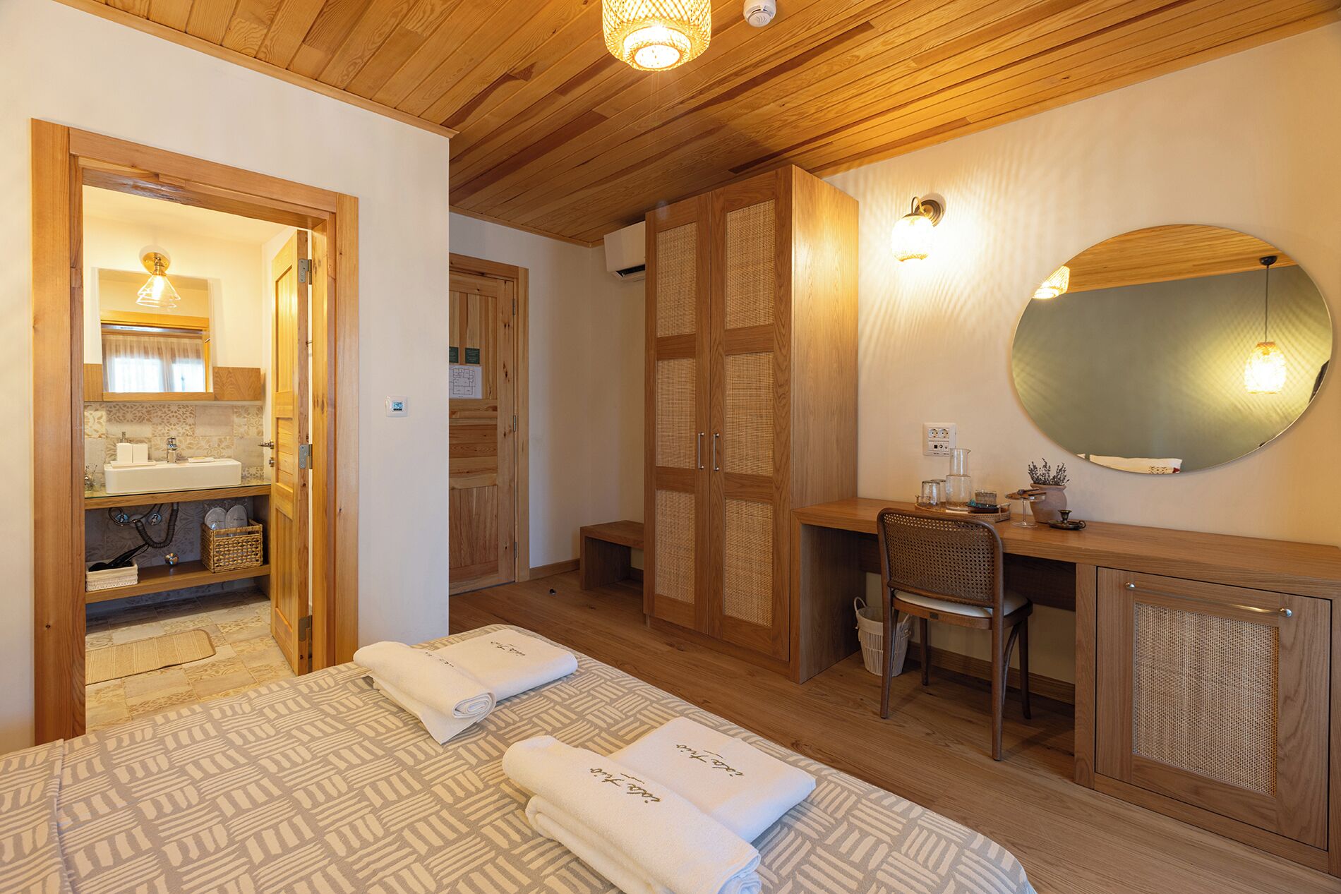 Une chambre à coucher comprenant un lit, un bureau, une chaise, un miroir, ainsi qu’une salle de bain avec un lavabo et un porte-serviettes.