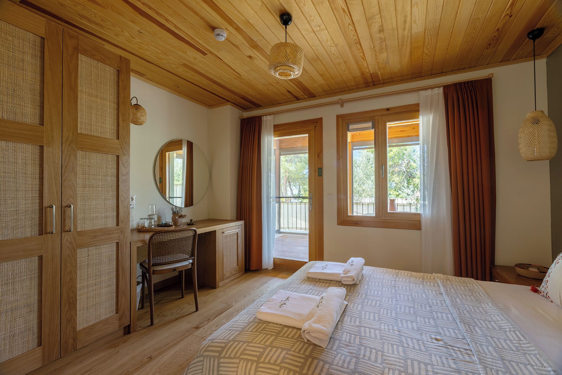 Una habitación con techo de madera, un escritorio con espejo, dos camas con toallas y vistas al exterior a través de ventanas.