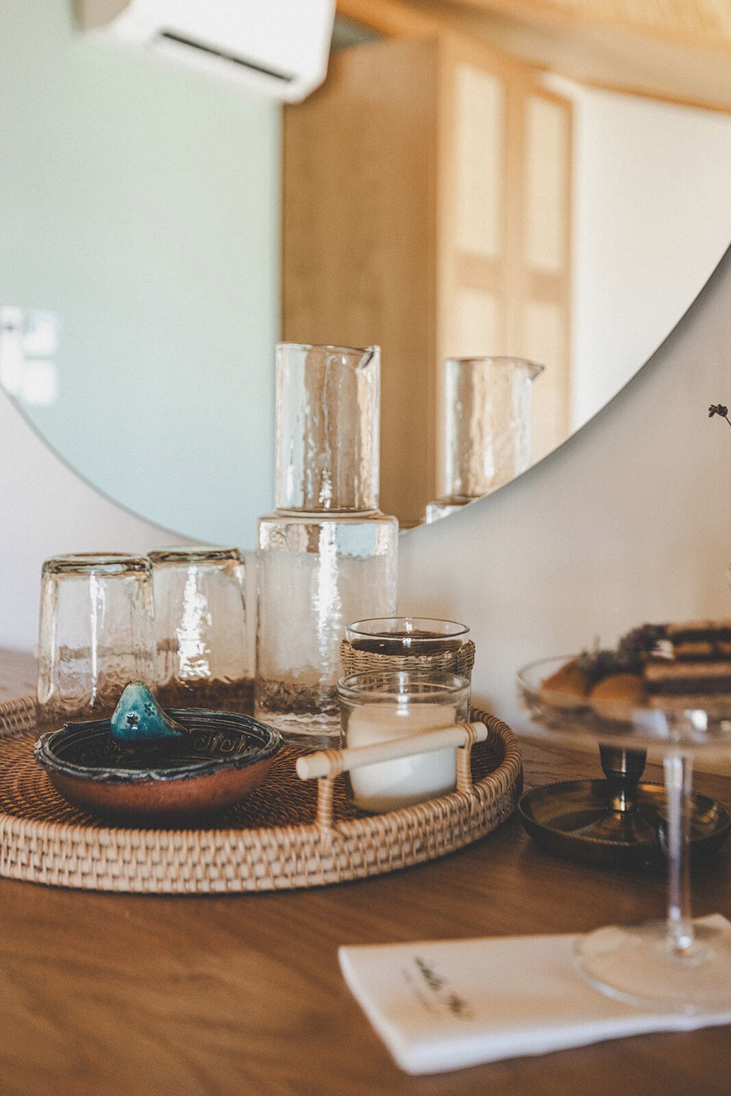 Une table ronde en bois, ornée de photophores en verre, une bougie et une petite assiette.