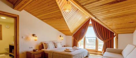 A cozy bedroom with a sloped ceiling, a bed with a patterned bedspread, bedside lamps, and a window with curtains.