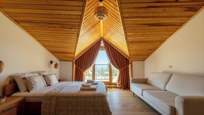 A bedroom with a bed, a sofa, a hanging light fixture, and a window with curtains. - Ida Trio (Edremit)