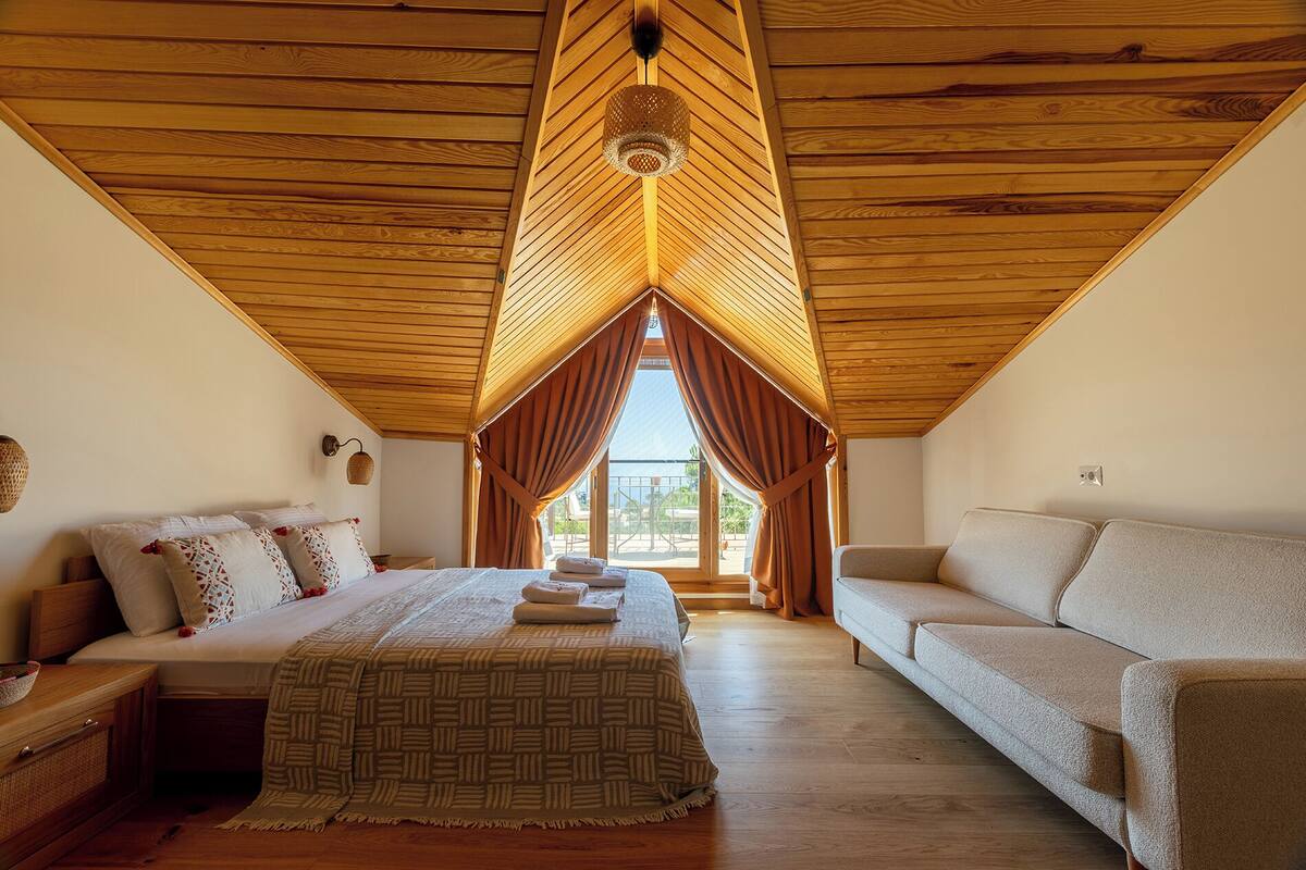 A bedroom with a bed, a sofa, a hanging light fixture, and a window with curtains.