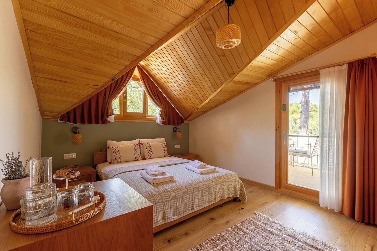A cozy bedroom with a sloped ceiling, a large bed, a wooden desk, and a window with curtains.