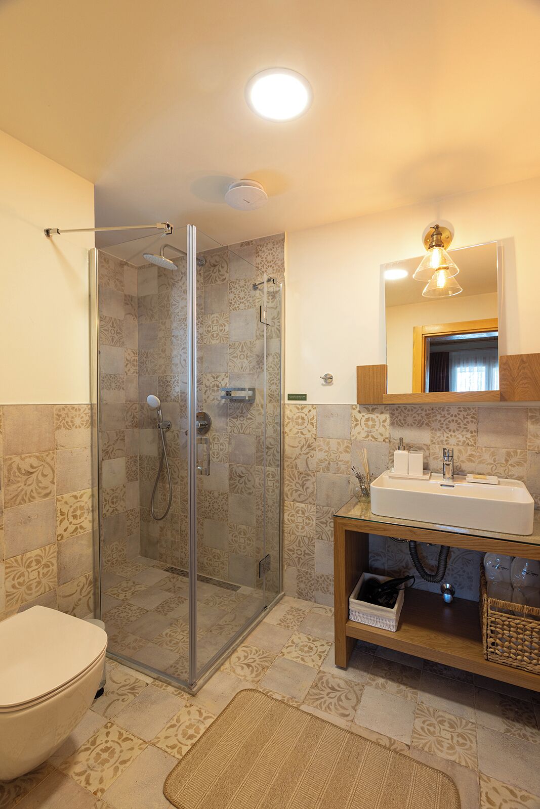 Un bagno con cabina doccia in vetro, un water, un lavandino con specchio sopra e piastrelle decorate su pareti e pavimento.