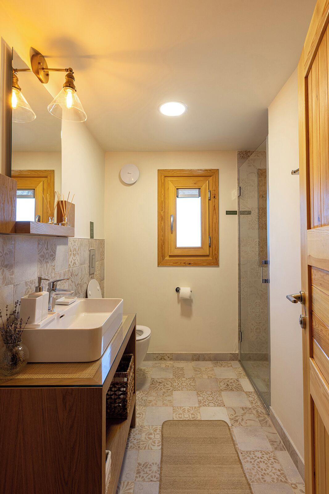 Een moderne badkamer met een houten wastafelmeubel, een grote spiegel, een toilet en een douchehoek.