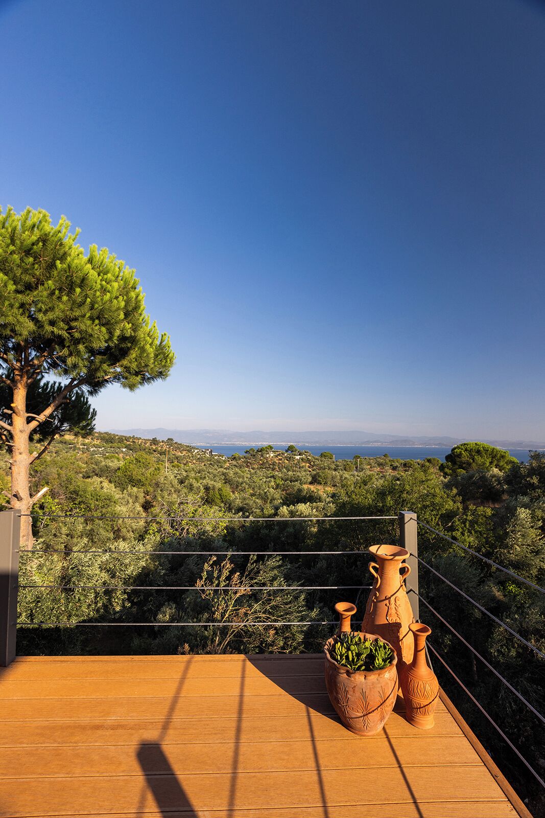 Eine Holzterrasse mit Terrakottatöpfen und Blick auf eine Küstenlandschaft.