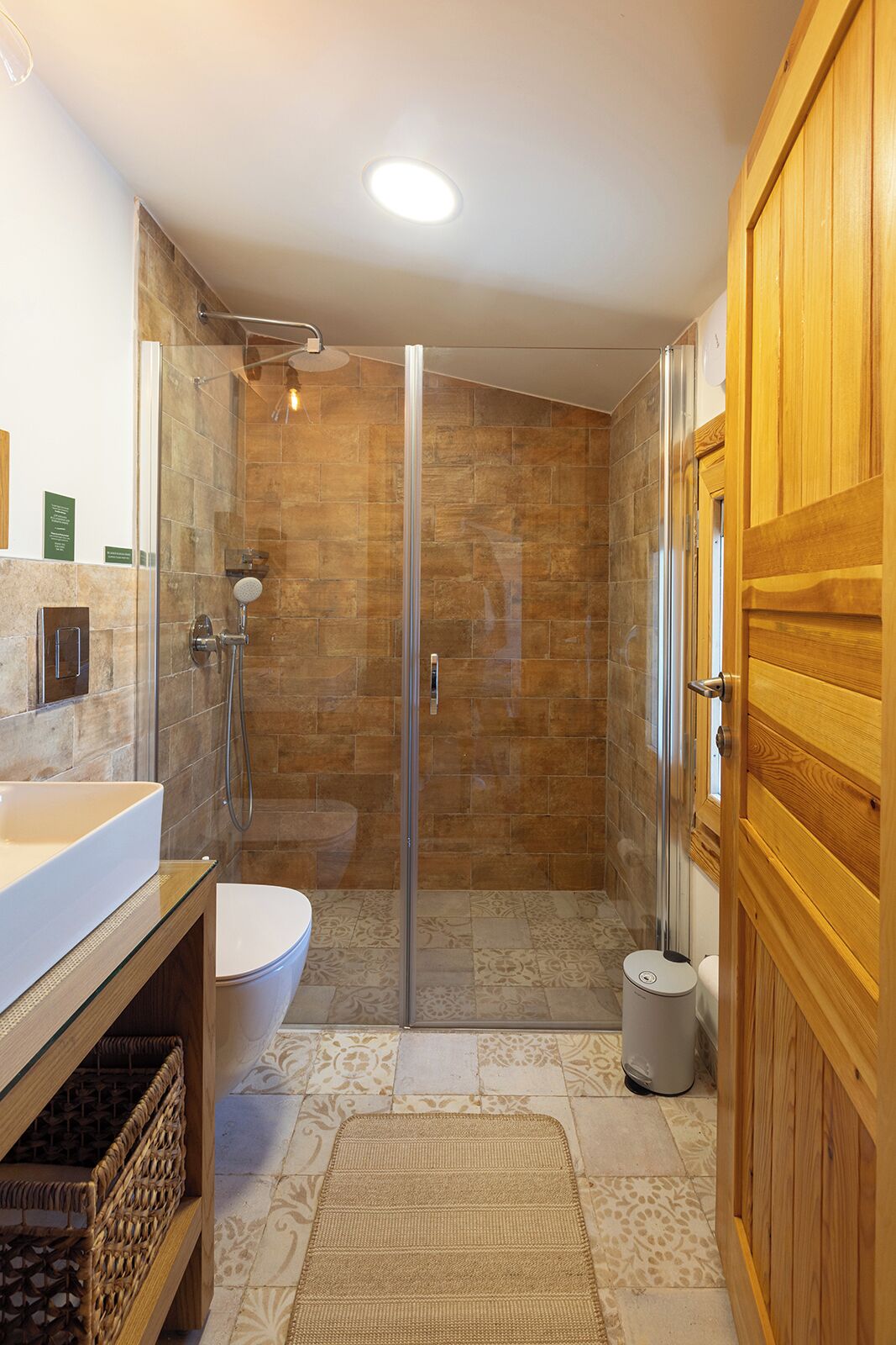 Un baño moderno con cabina de ducha de vidrio, un lavabo blanco y una puerta de madera.