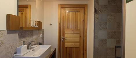 A bathroom with a wooden door, a white sink, and a shower area.