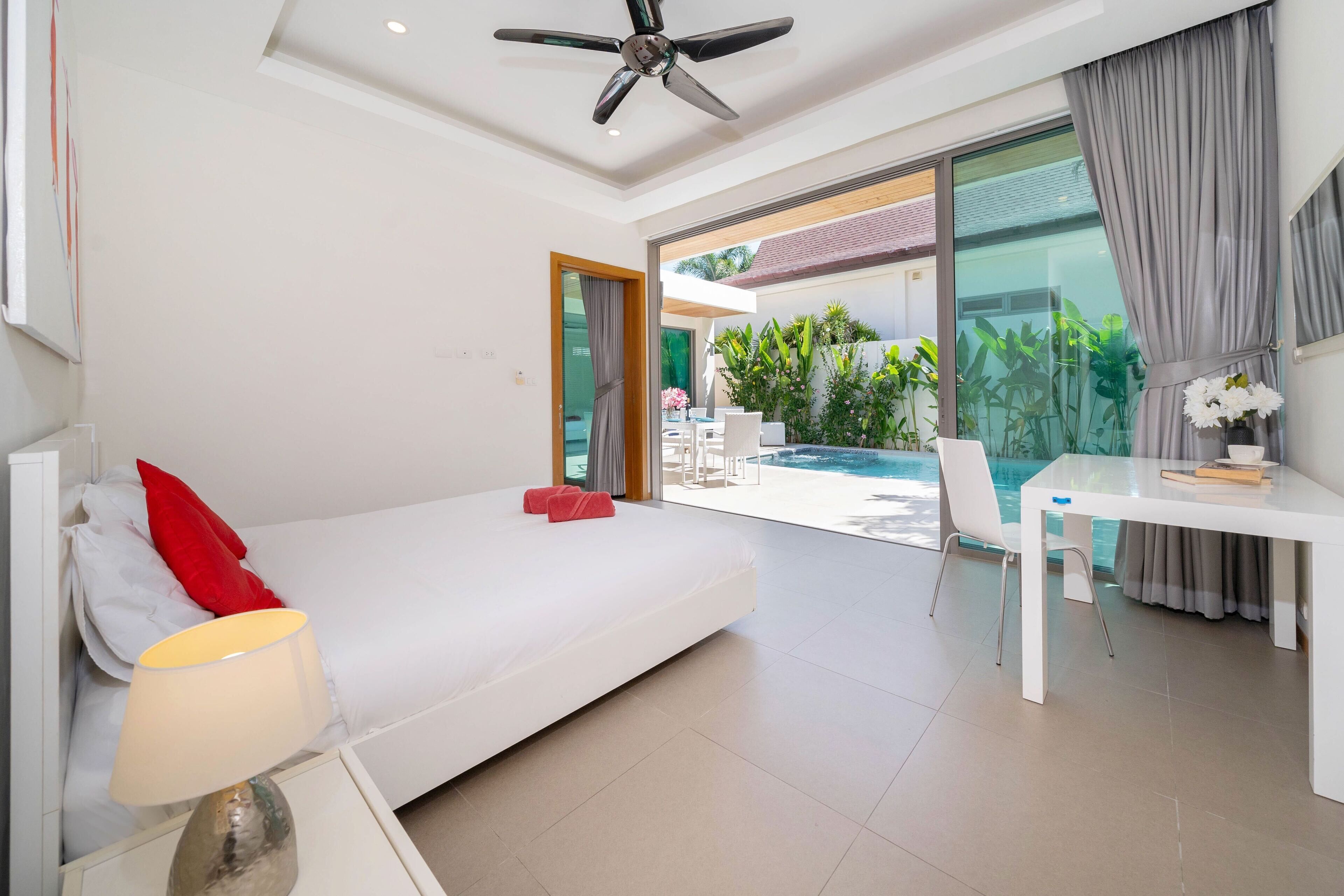 A modern hotel room with a bed, a desk, a chair, a lamp, and a ceiling fan.