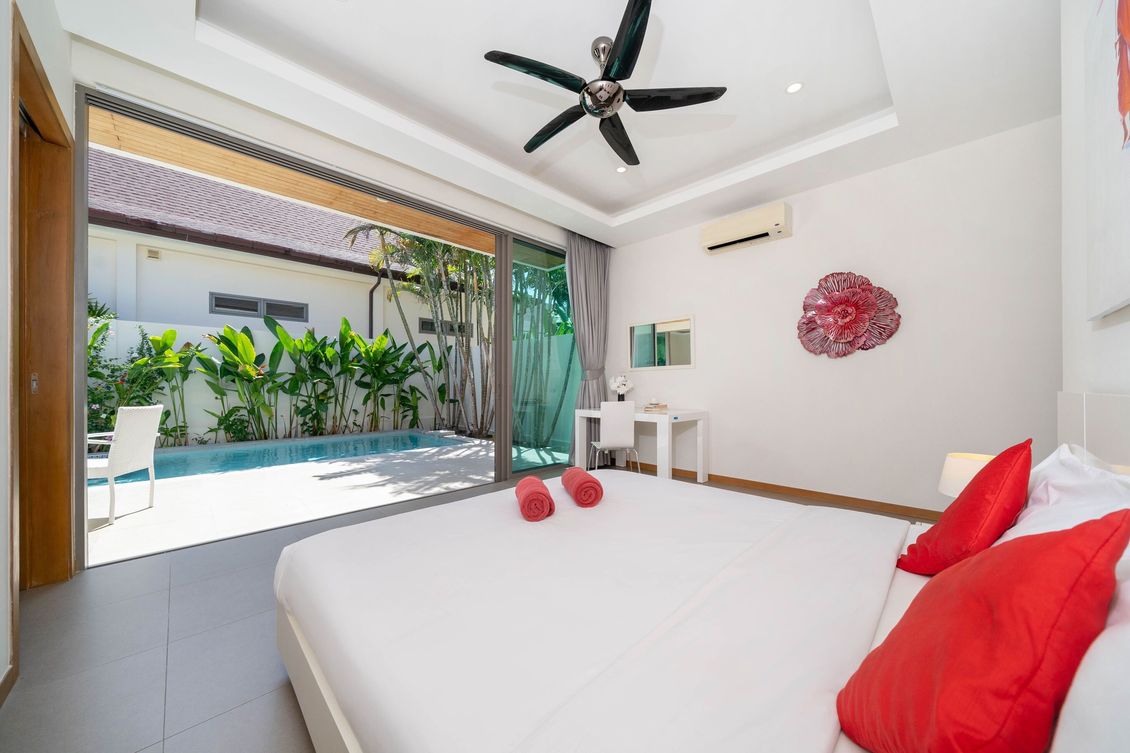 A modern hotel room with a large bed, a ceiling fan, a small desk, and a view of a swimming pool.