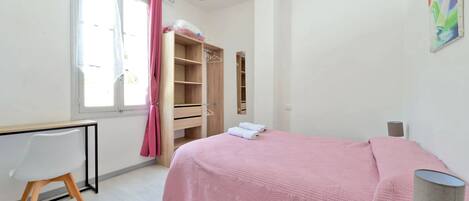 A bedroom with a bed, a desk, a wardrobe, and a window with curtains.